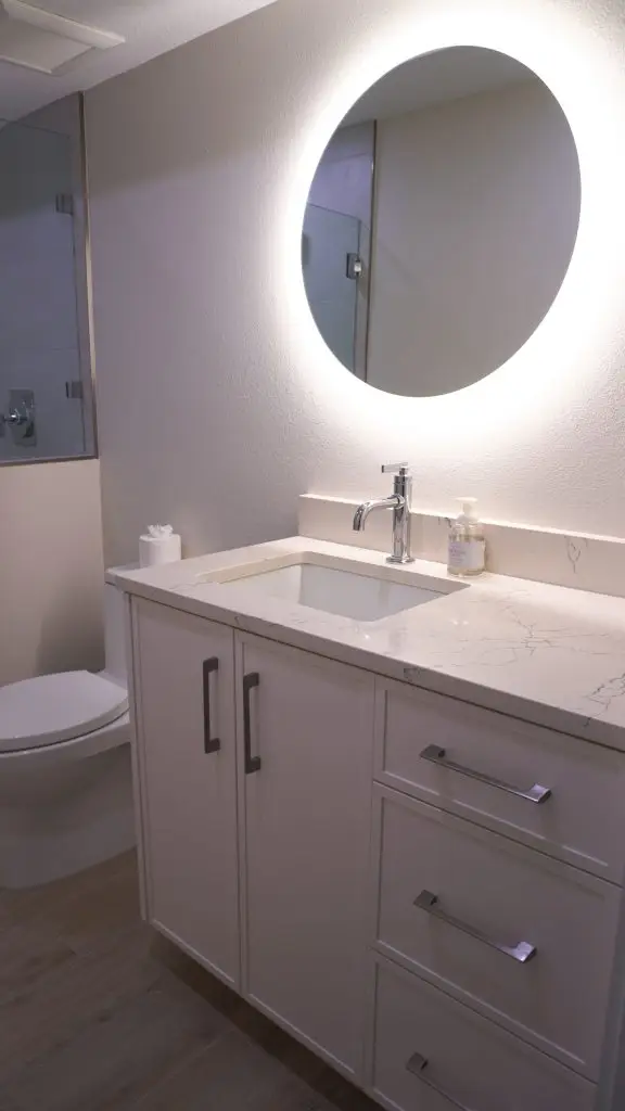 Guest bathroom in a Longboat Key apartment unit, featuring a modern mirror with integrated LED lighting—part of Florida Design Works’ recent renovation project.